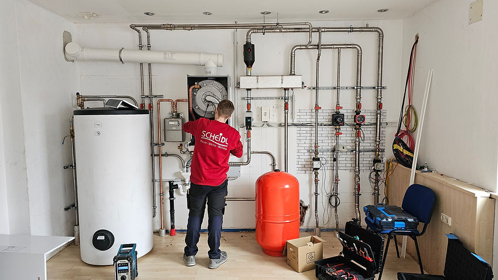 Installateur arbeitet an Heizungsanlage mit Rohren, Pufferspeicher und Steuerungseinheit in Technikraum.