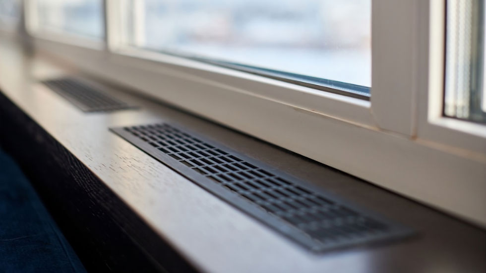 Dunkelbraune Fensterbank vor einem Fenster mit weißen Rahmen. Unter dem Fenster befindet sich ein schwarzes Belüftungsgitter.