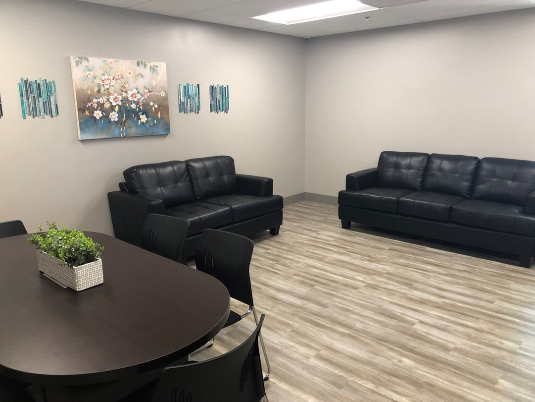 A warm, cream and khaki-colored lounge with a black leather sofa and loveseat placed to the right of a dark brown dining room table. 