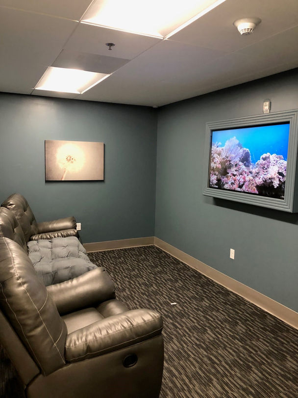 A living room, featuring three large brown leather accent chairs placed in front of a flat screen TV. This room is characterized by sky blue walls and soft, low pile dark brown carpet.