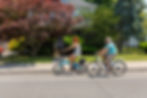 Seniors riding ebikes on street past home with trees in yard
