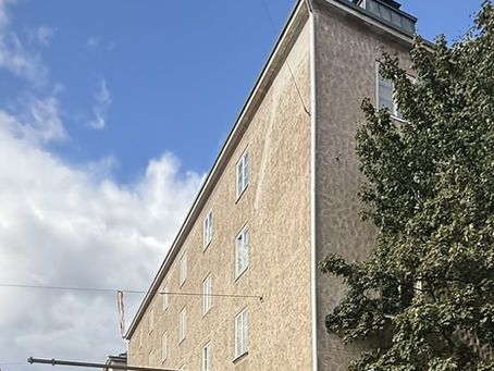 Vaalea kerrostalo Helsingin katuympäristössä sinisen taivaan alla.