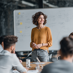 Female educator leading a professional development session, standing in front of a whiteboard and engaging a group of teachers.