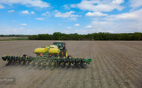 Tractor moving forward, tilling field with dust kicking up. Clouds over a blue sky.