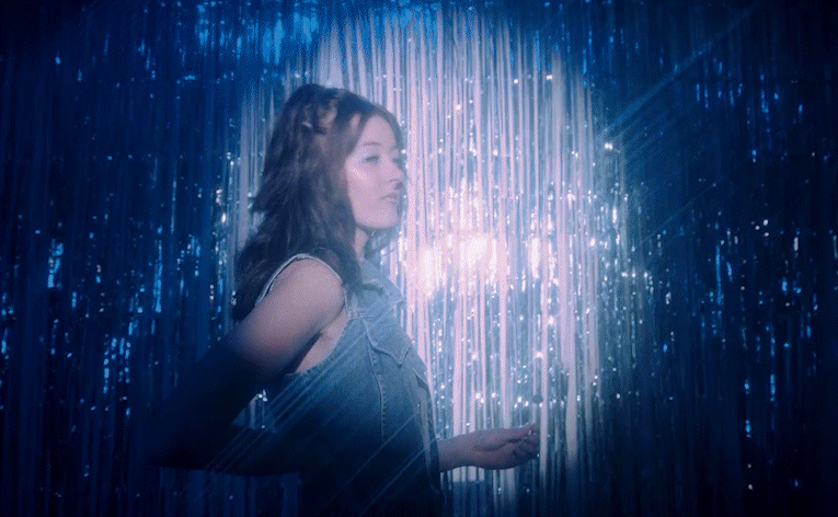 A gif of a young model sucking on a lollipop against a bedazzled blue background.