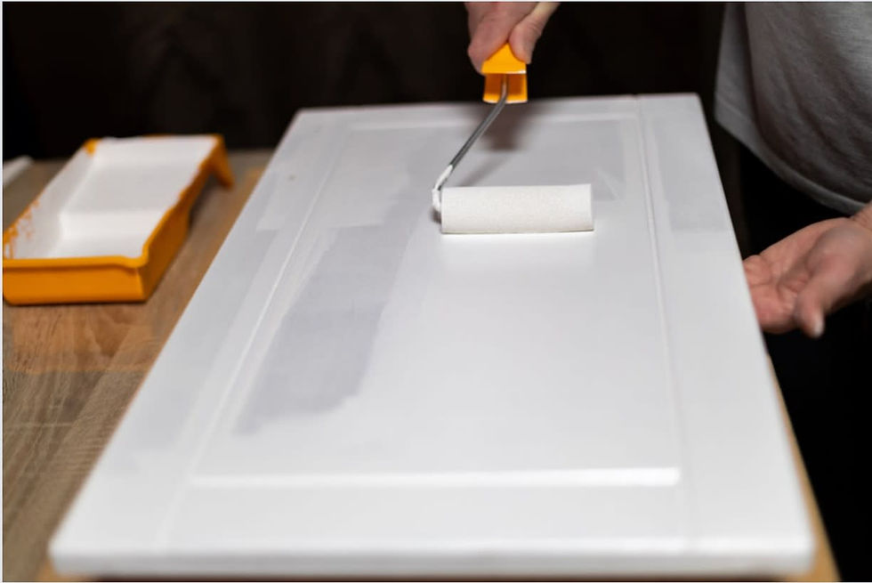 A_person_using_a_paint_roller_to_apply_fresh_coat_of_white_paint_to_a_cabinet_door_y0f445.