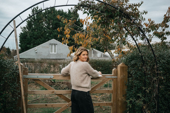 Garden designer standing at a wooden gate framed by plants and climbing greenery