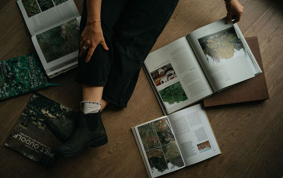 Person sitting on a wooden floor surrounded by open gardening and landscape design books, viewed from above.