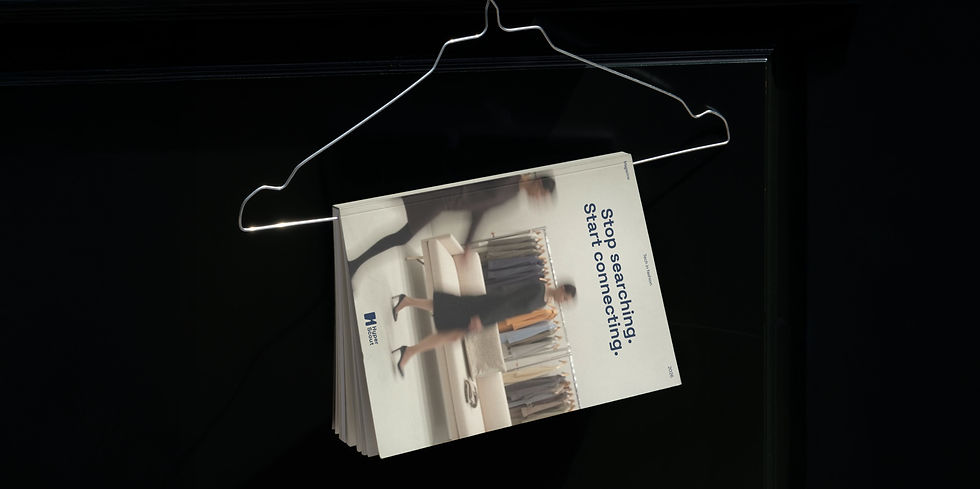 Stack of Hyperscout brochures hanging on a metal clothes hanger against a dark background, featuring the text “Stop searching. Start connecting.”