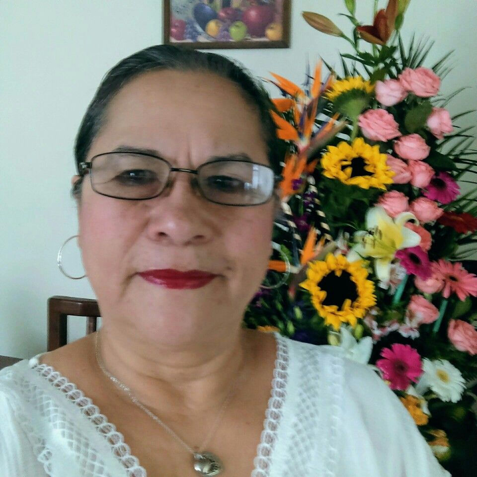 Mujer sonriente con gafas frente a un arreglo floral.