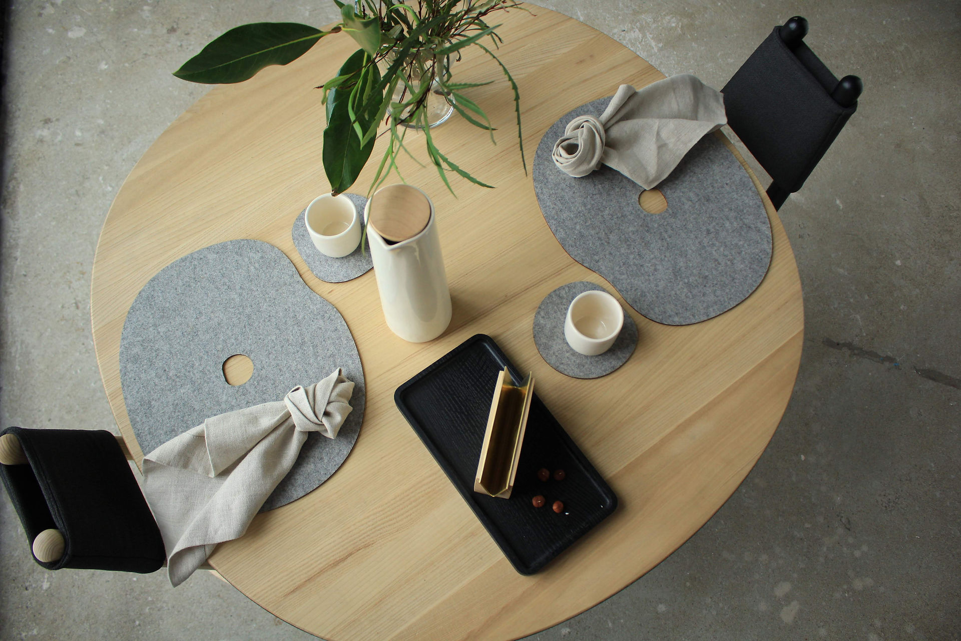 Table mat MILLSTONES by Namuos on a wooden table with napkins and a black plate, porcelain cups and vase