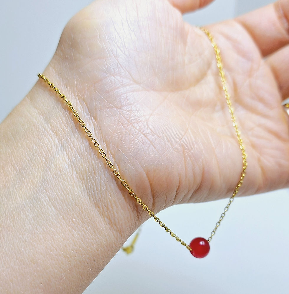 Indexkép: an elegant golden necklace with a red glass bead on a hand