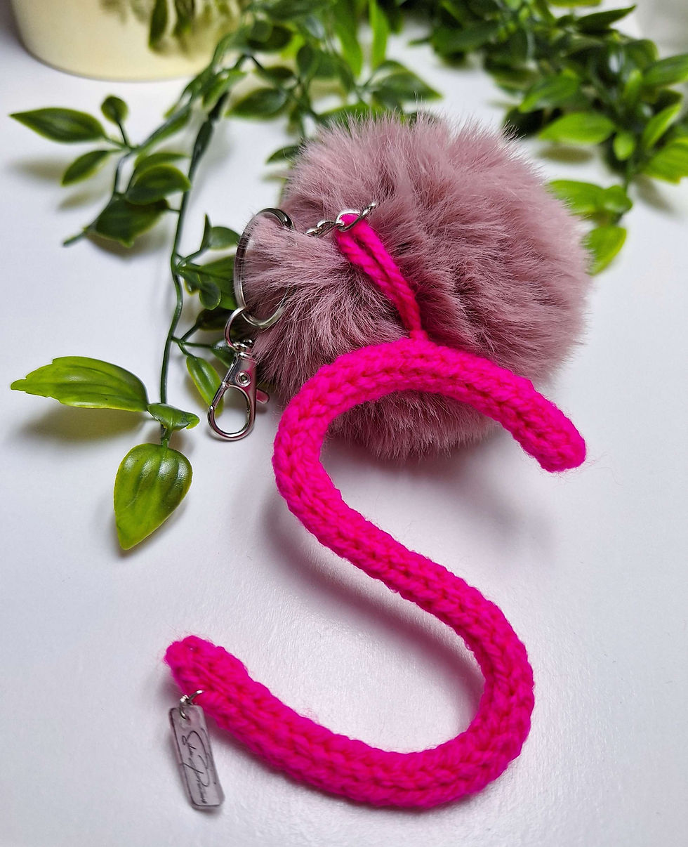 الصورة المصغرة: closer up view of fuchsia  knitted letter S and pink pompom handmade keychain with some green snake plants at the back