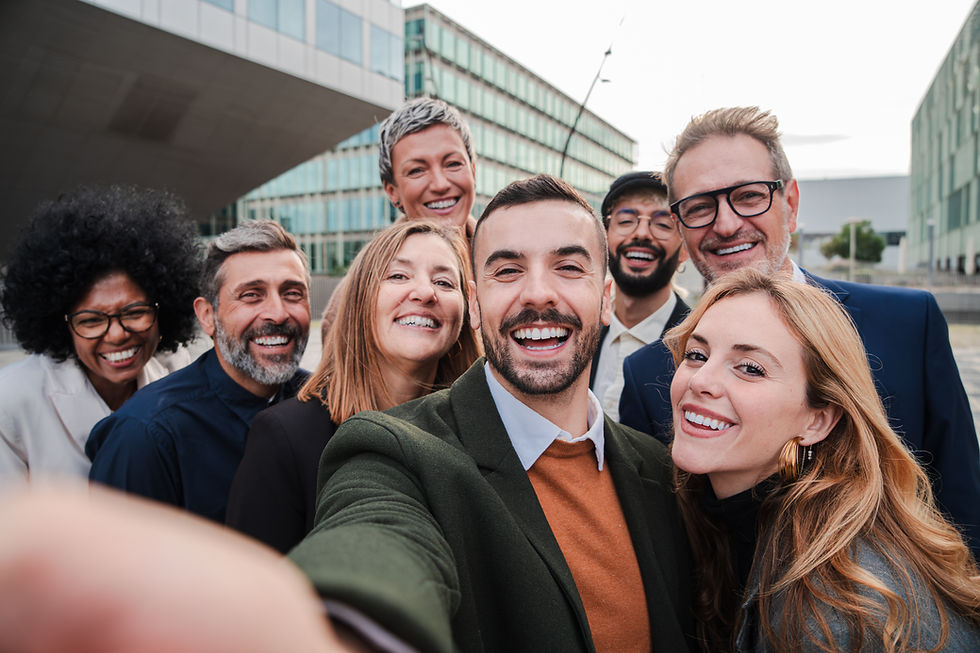 A diverse group of eight people smiling for a selfie outdoors. Modern building in the background, conveying a joyful and friendly mood.