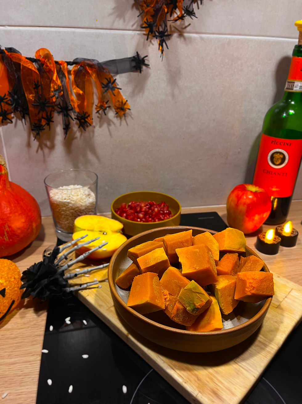 Ingredienti per il risotto alla zucca, mela e melagrana di Halloween ispirato a Capo Plaza Hustle Mixtape 2: zucca a cubetti, mele, melagrana, riso e vino rosso in cucina decorata a tema.