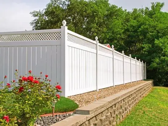 White vinyl fence with lattice top bordering a landscaped garden and retaining wall