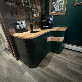 Custom curved dark green bar cabinet with fluted fronts and light ash countertop with tap and fridge by Chisel Woodworking in London, Ontario