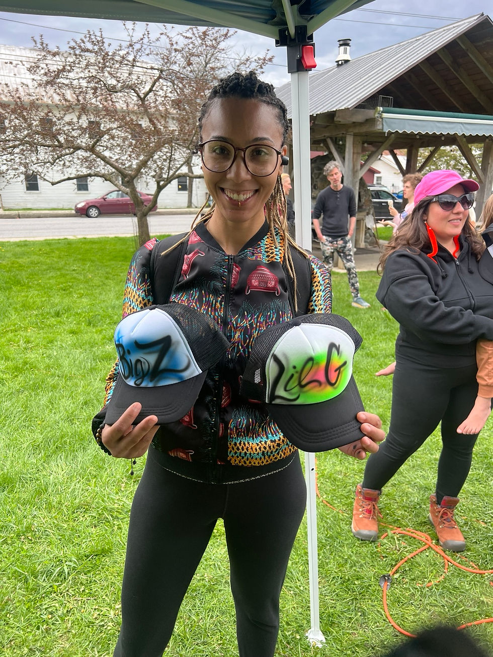 Guest holding two colorful custom airbrushed hats at a Vermont State University campus event