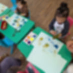 Two young children painting, one wearing 'POP' shirt, at green tables.