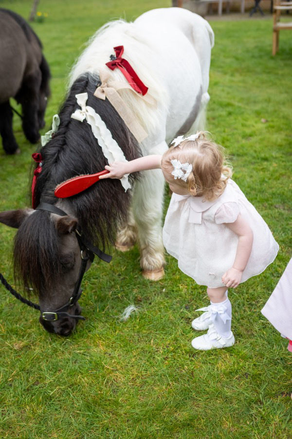 Young girl brushing a pony; white dress, red bow, garden scene. Magic Ponies