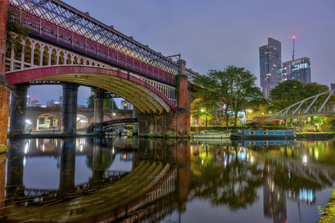 Ornate railway bridge over Manchester canal at twilight with reflections.
