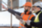 Two construction workers in safety vests pointing at something, discussing plans.