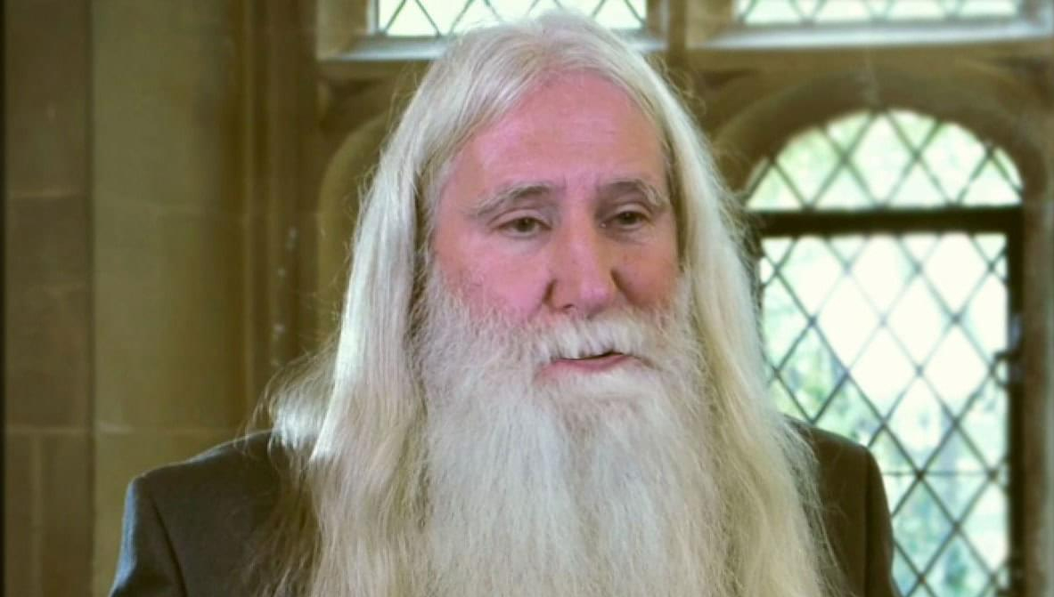 Elderly man with long white hair and beard in a building.