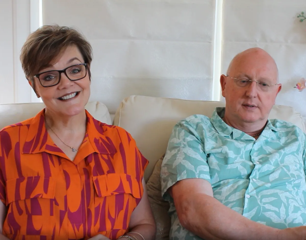 Smiling woman and man sitting comfortably on a white couch together.