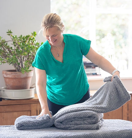 Woman folding gray towels on a table, plants visible in the background, Stay Strong Massage.