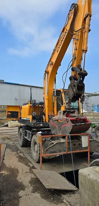 Yellow excavator at construction site. Demolition work in progress near a building.