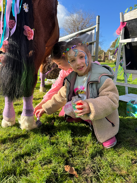 Girl with face paint paints horse's wrapped hoof