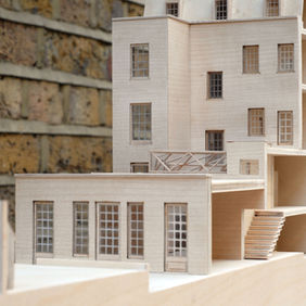 Wooden architectural model of a multi-story building against a brick wall.
