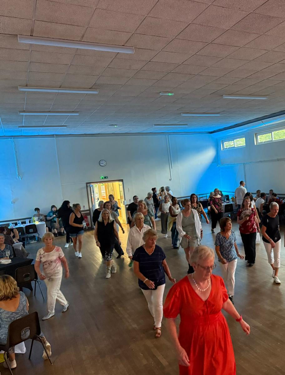 Many adults dancing or exercising indoors under blue stage lights.