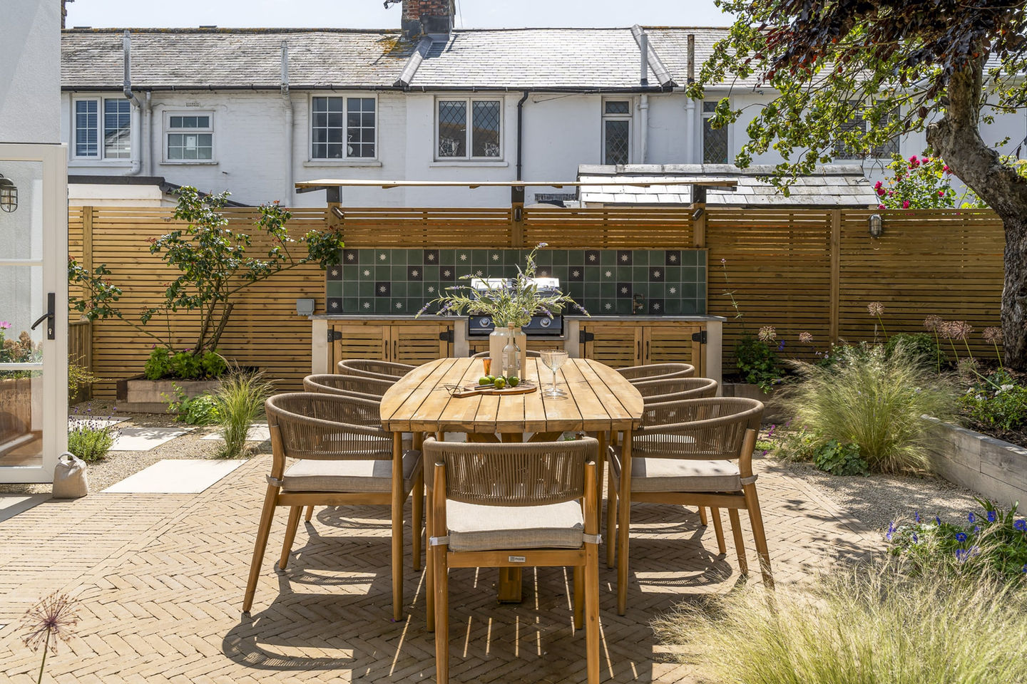 Outdoor patio dining set with wooden table, chairs, and garden background. AC Gardens