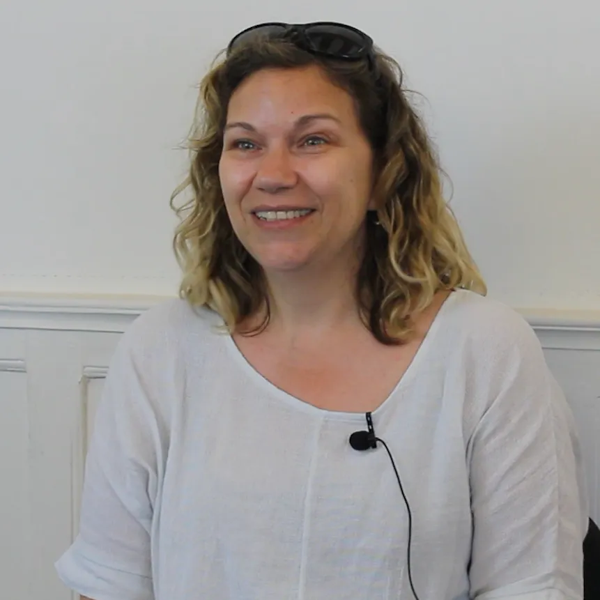 Smiling woman with curly hair wearing white top and small microphone.
