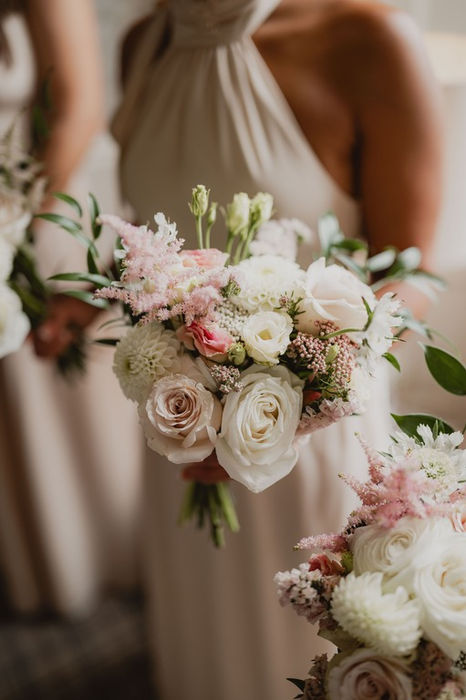 Bridesmaids holding bouquets of white and pink flowers in neutral dresses.