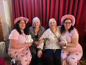 Four happy women in pink pajamas and hats, holding teddy bears.