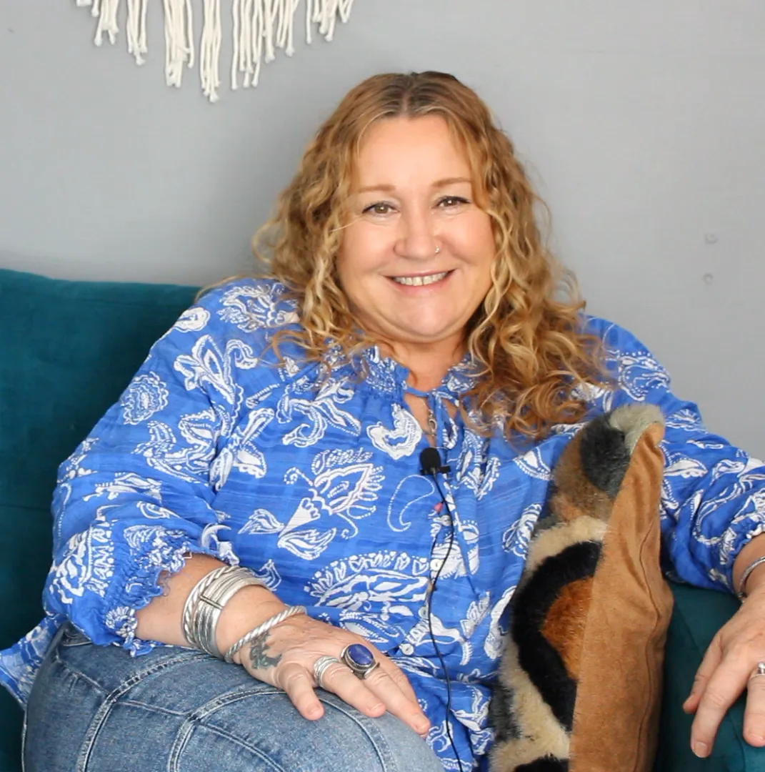 Smiling woman with long blonde hair in blue shirt on teal sofa.