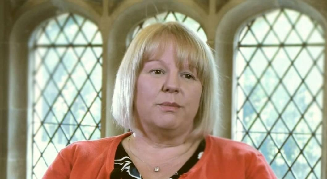 Professional blonde woman in coral cardigan, ornate latticed window background.