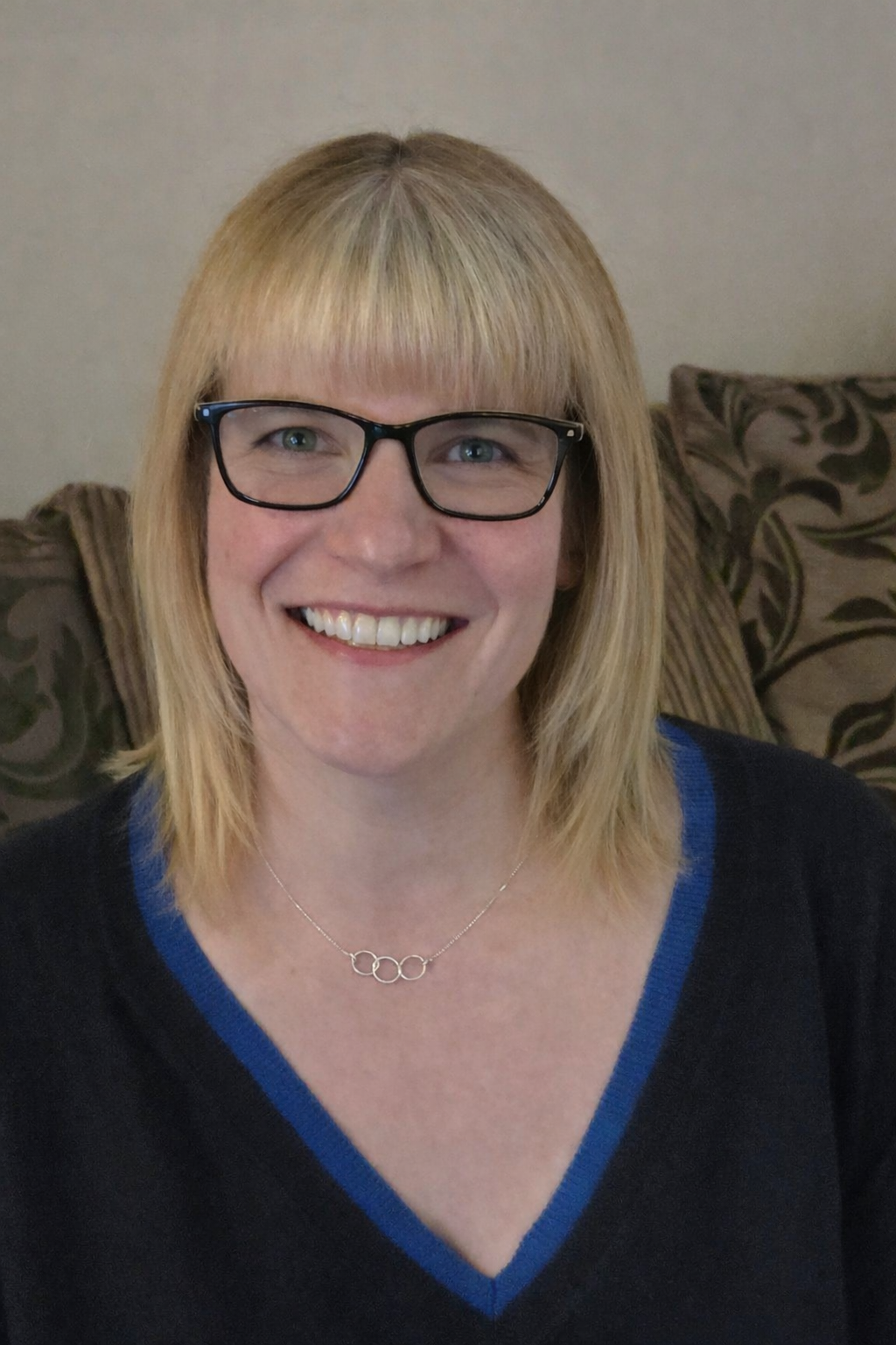 Smiling woman with blonde hair, glasses, and blue top.