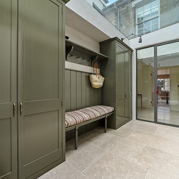 Bright entryway with sage green cabinets, bench, and glass doors