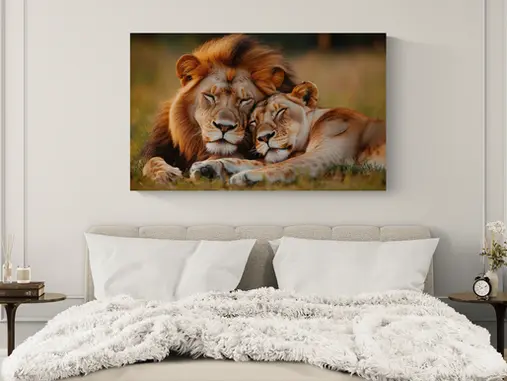Resting lion and lioness canvas wall art centered above an upholstered bed in a calm neutral primary bedroom with soft white bedding, warm taupe tones and balanced bedside tables.
