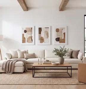 Warm neutral modern living room styled for fall with an ivory sectional, layered beige textiles, minimalist abstract wall art, natural wood accents and indoor greenery