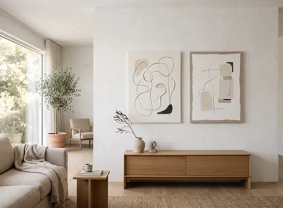 Calm minimalist living room displaying gallery-wrapped canvases with sparse black line work and soft neutral shapes against warm white walls.