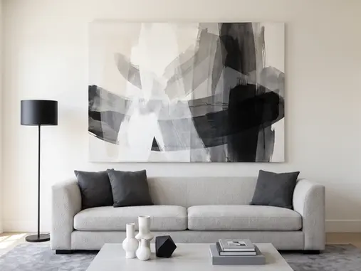 Bright contemporary living room featuring oversized black, white and gray monochromatic abstract gallery-wrapped canvas above a light-gray sofa, showing how tonal contrast, layered brushwork and varied values add depth to minimalist décor.