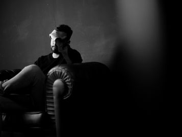 Man in emotional reflection sitting on a couch, shadow cast behind him, symbolizing inner conflict and betrayal trauma.