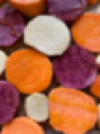 Süßkartoffelscheiben legen nebeneinander auf einem Blech, die Süßkartoffeln sind weiß, orange und lila