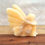 Thumbnail: Orange calcite fairy in seated position with legs crossed and folded arms with wings straight behind