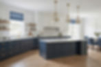 Spacious American kitchen featuring white upper cabinets, a large navy blue island, and gold pendant lights with marble countertops.