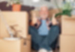 Happy senior man sitting among moving boxes giving a thumbs up, representing stress-free senior moving assistance and downsizing support